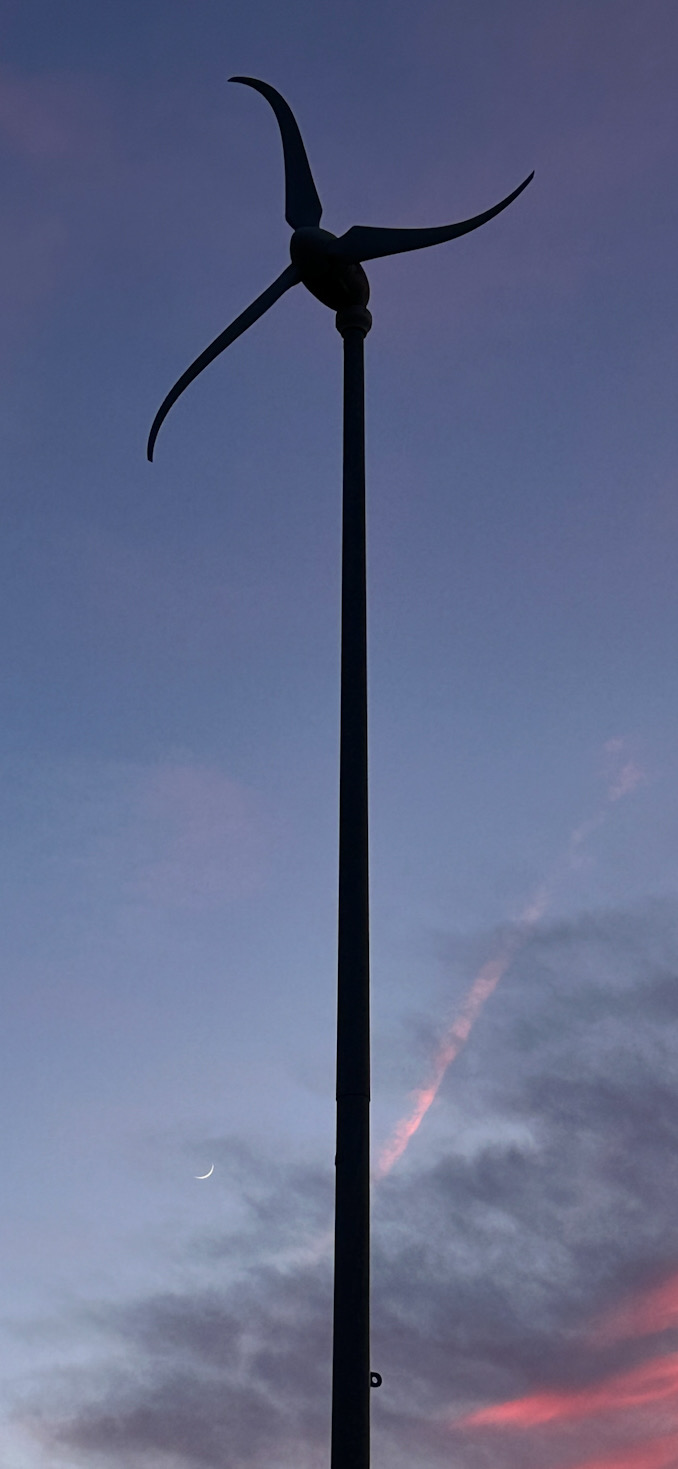 Photo at Thomas Middle School, captured at 8:43 p.m. Saturday, June 8, 2024, showing a Skystream 3.7 Wind Turbine, capable of generating power from wind, with a waxing crescent moon in the background (CARDINAL NEWS)