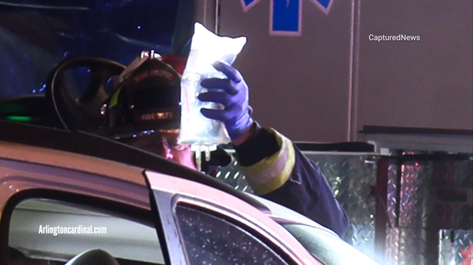 A Mount Prospect Fire Department firefighter/paramedic holds a medical IV solution bag during extrication of a patient in a white SUV on Rand Road north of Euclid Avenue in Arlington Heights after a head-on crash Monday night, September 2, 2024 (CARDINAL NEWS)