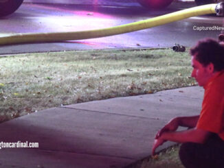 Evan Rude crouching near a sidewalk across the street from his family's house after a fire he is accused of starting caused over $300,000 damage (CARDINAL NEWS)