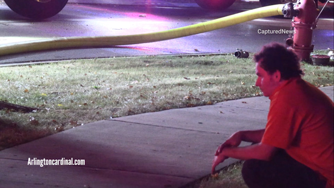 Evan Rude crouching near a sidewalk across the street from his family's house after a fire he is accused of starting caused over $300,000 damage (CARDINAL NEWS)